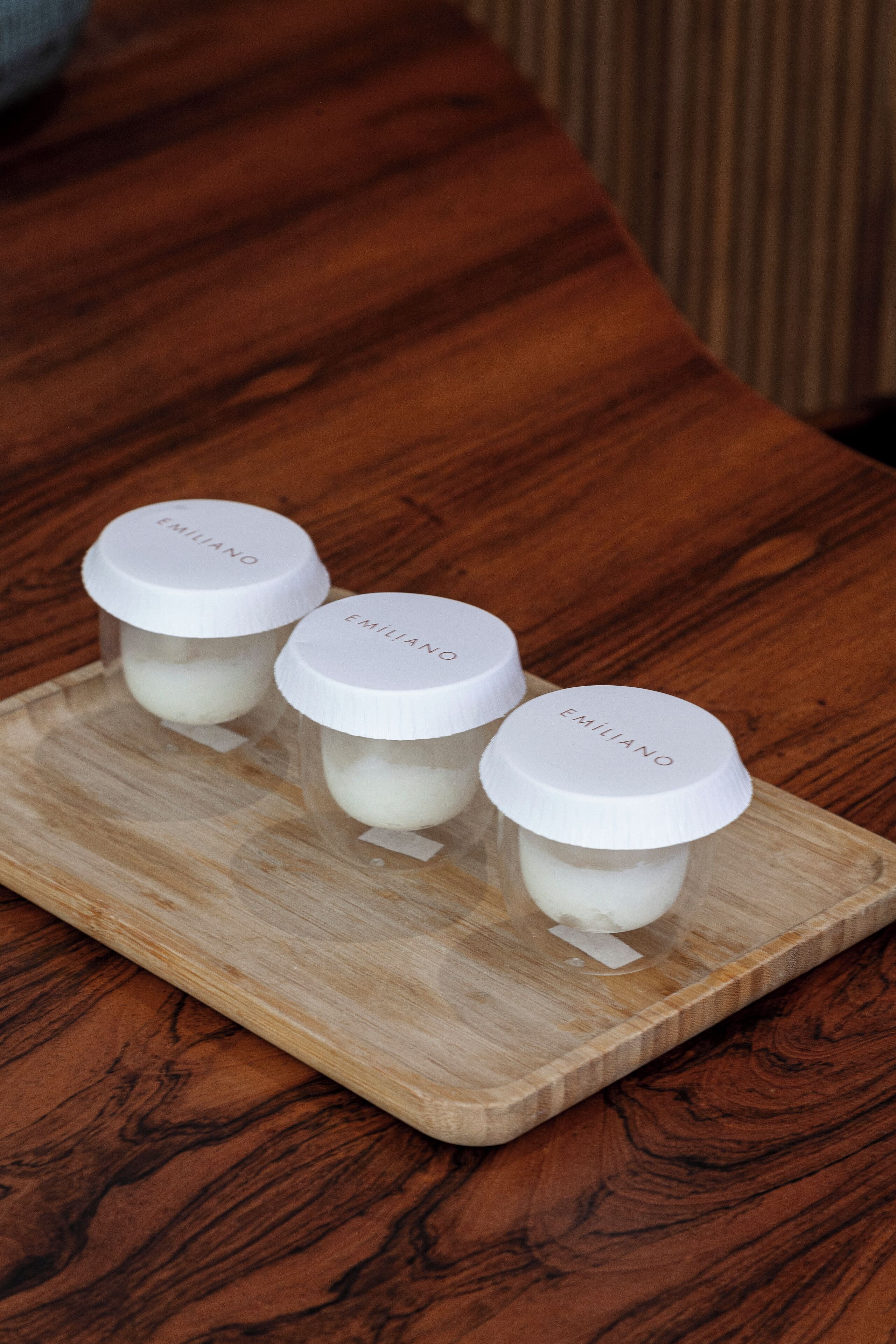 Tres frascos con tapas blancas sobre una bandeja de madera.