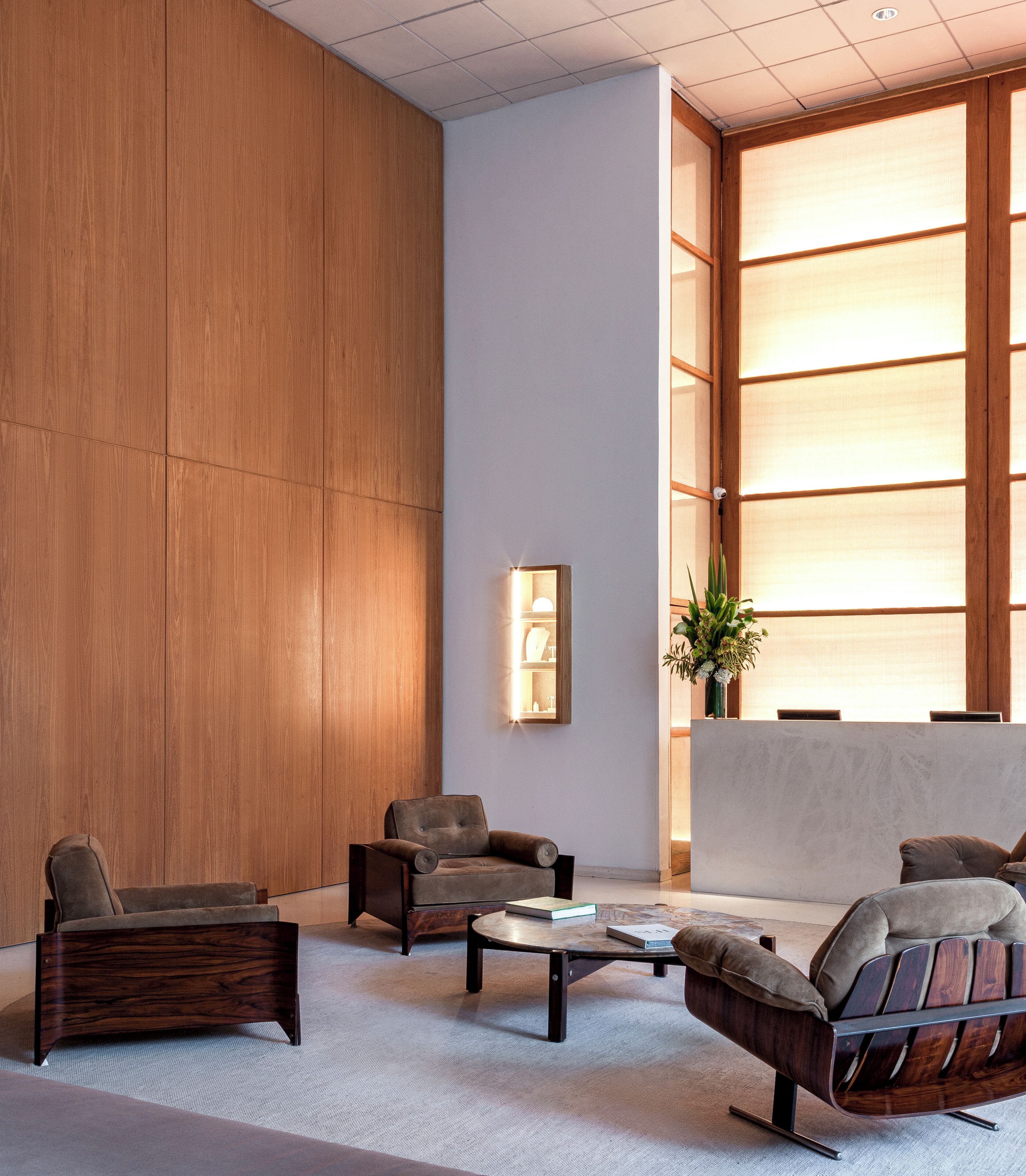 A modern lobby with wooden panel walls, a reception desk, and seating areas with sofas and a coffee table.