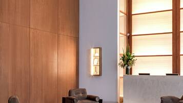 A modern lobby with wooden panel walls, a reception desk, and seating areas with sofas and a coffee table.