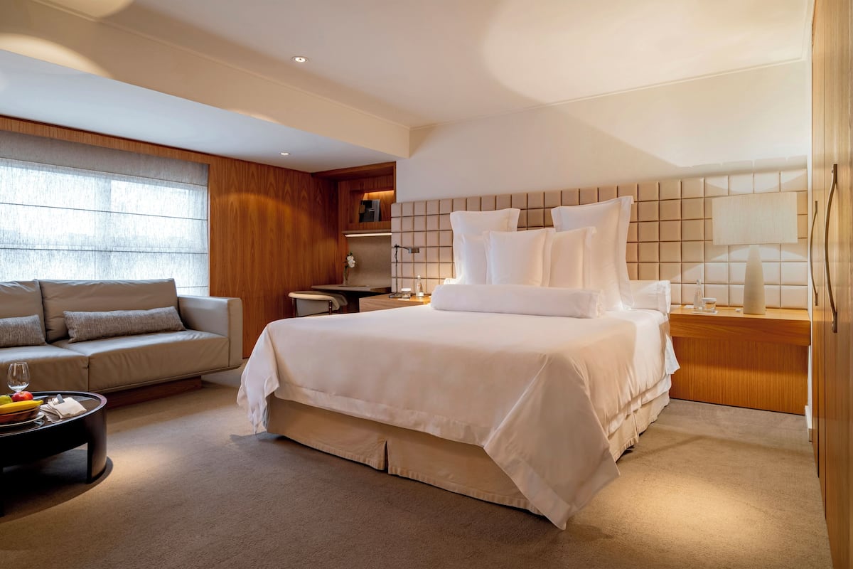 Ein modernes Hotelzimmer mit einem großen Bett, einer Couch, einem Couchtisch mit Obst und Blick auf die Stadt.