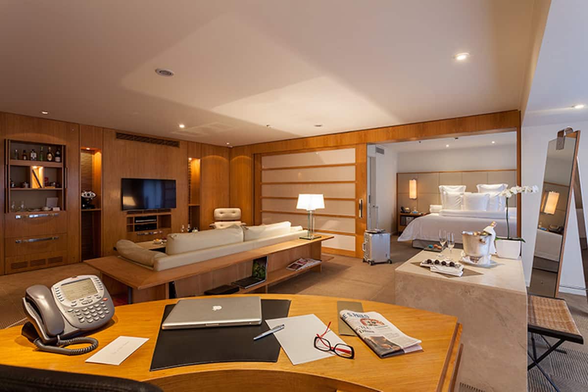 Ein Hotelzimmer mit Schreibtisch, Telefon, Laptop und einem Bett mit Nachttisch.