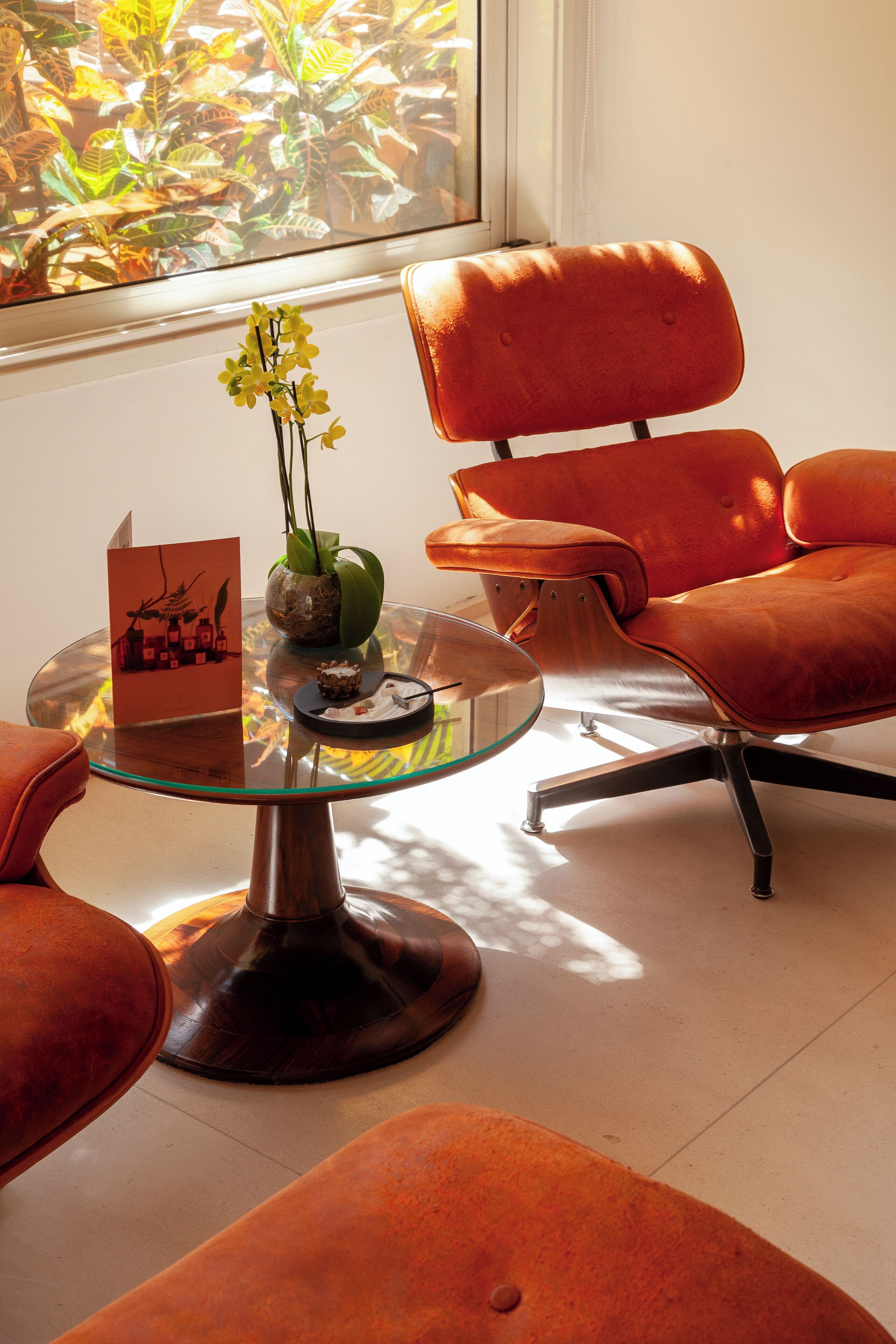 Una habitación moderna con una mesa de vidrio, sillas naranjas, un jarrón con flores y una tarjeta sobre la mesa.