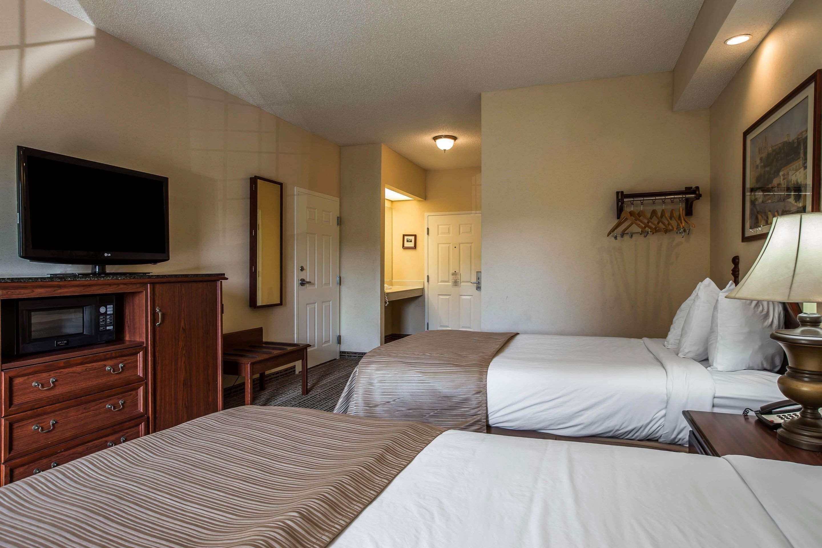 A hotel room with two beds, a television, a desk, and a lamp.