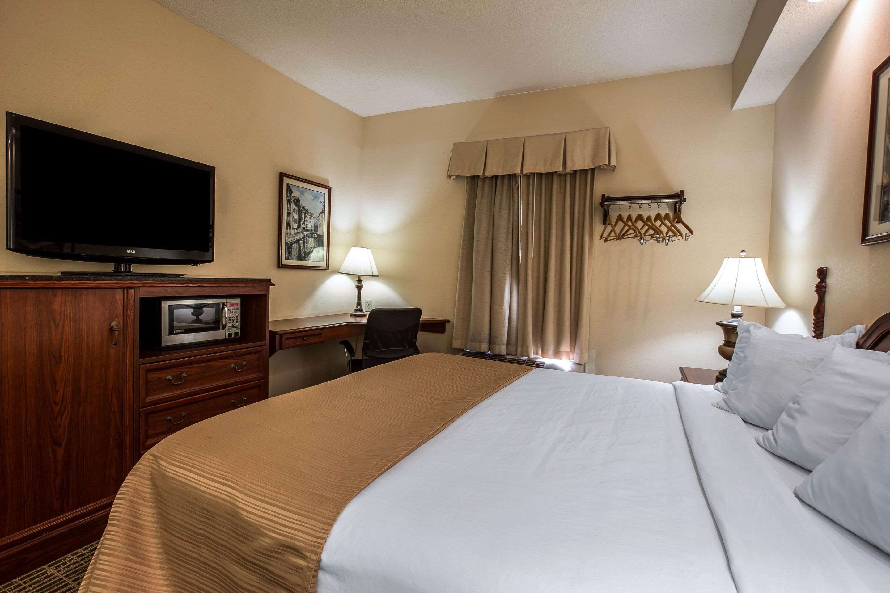 A hotel room with a large bed, a desk with a computer, a television, and a window with curtains.
