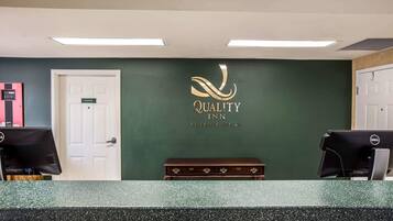 A reception desk with a green wall, a sign reading "Quality Inn by Choice Hotels," and two computer monitors.