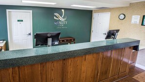 Un mostrador de recepción de hotel con una pared verde, un cartel que dice 'Quality Inn by Choice Hotels' y dos puertas cerradas con la leyenda 'Gerente'.