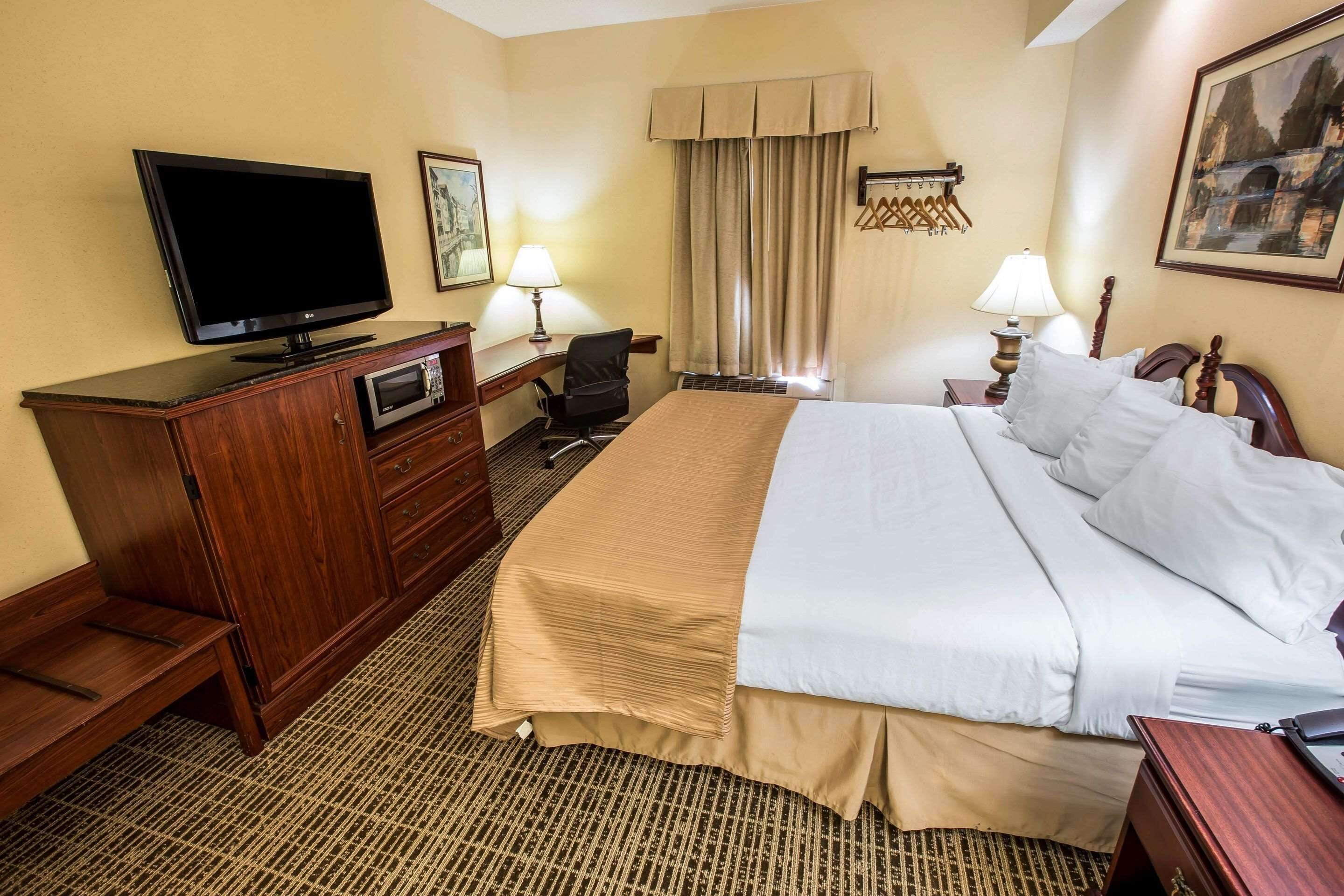 Een hotelkamer met een bed, een bureau met een computer, een televisie en een raam met gordijnen.