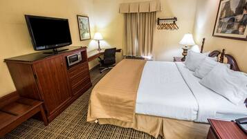 A hotel room with a bed, a desk with a computer, a television, and a window with curtains.