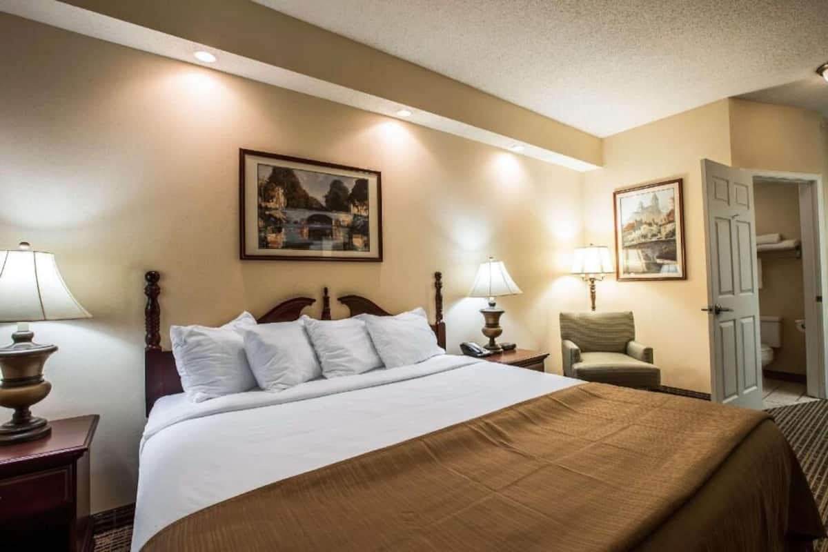 Une chambre d’hôtel comprenant un lit, deux lampes de chevet, une chaise et une porte donnant accès à la salle de bain.