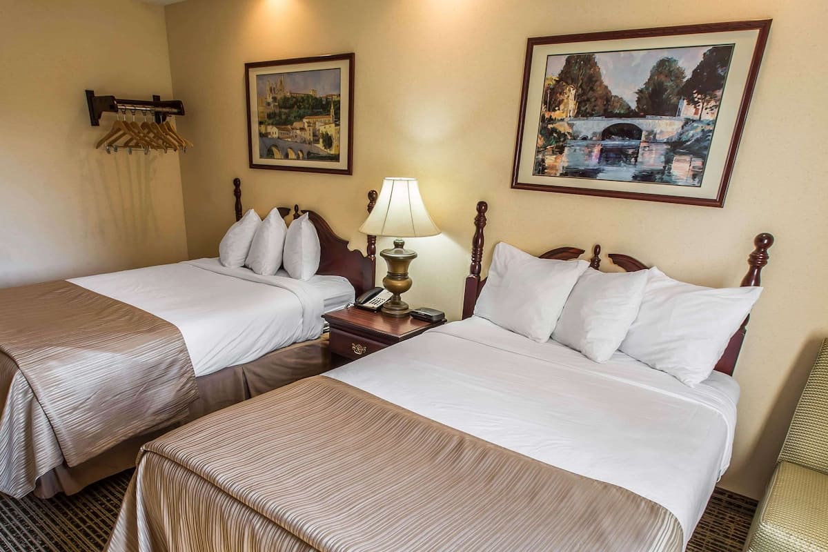 Une chambre d’hôtel avec deux lits, une table de chevet avec une lampe, un téléphone et un porte-manteau.