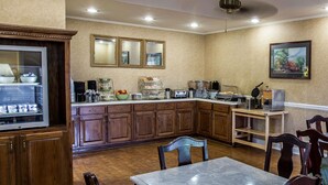 Una cocina con armarios de madera, un refrigerador, una estación de café y un comedor con mesa y sillas.