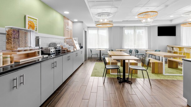 Une cuisine moderne avec un coin repas, des meubles en bois, un mur vert et un téléviseur à écran plat.