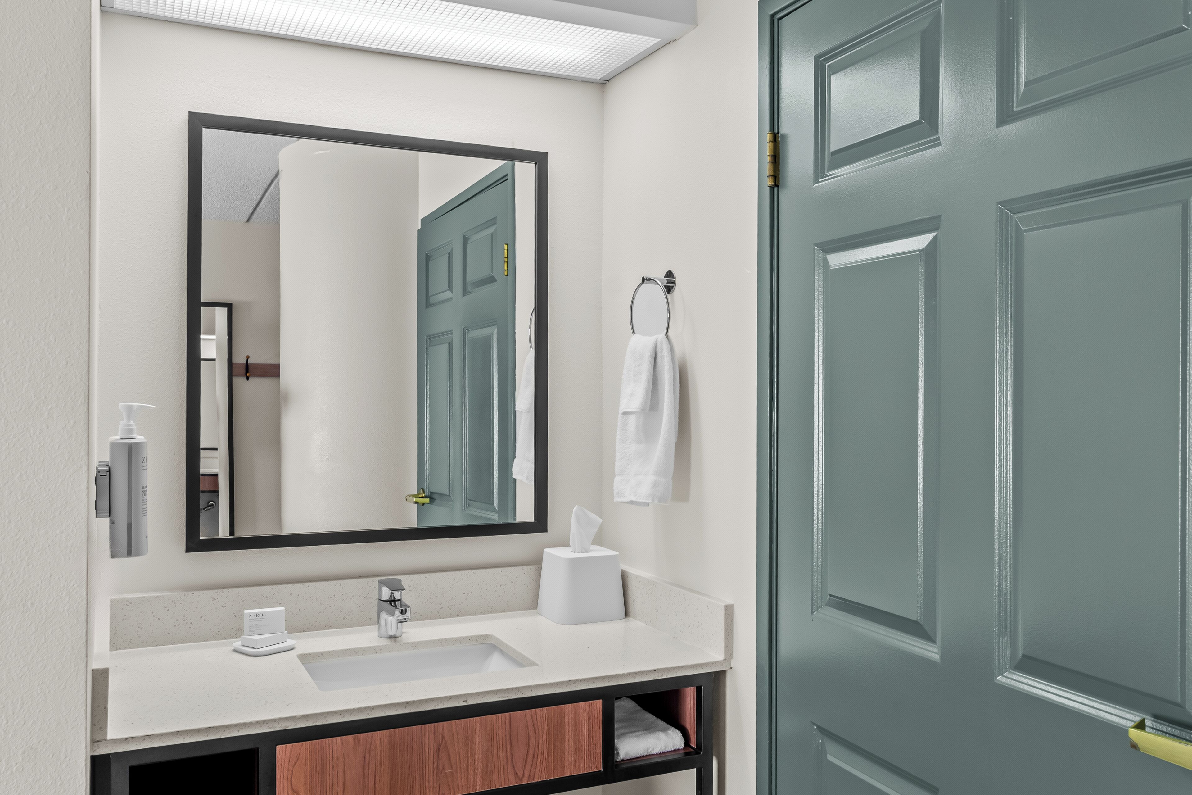 A bathroom with a mirror, sink, towel rack, and a door.
