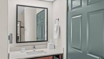 A bathroom with a mirror, sink, towel rack, and a door.