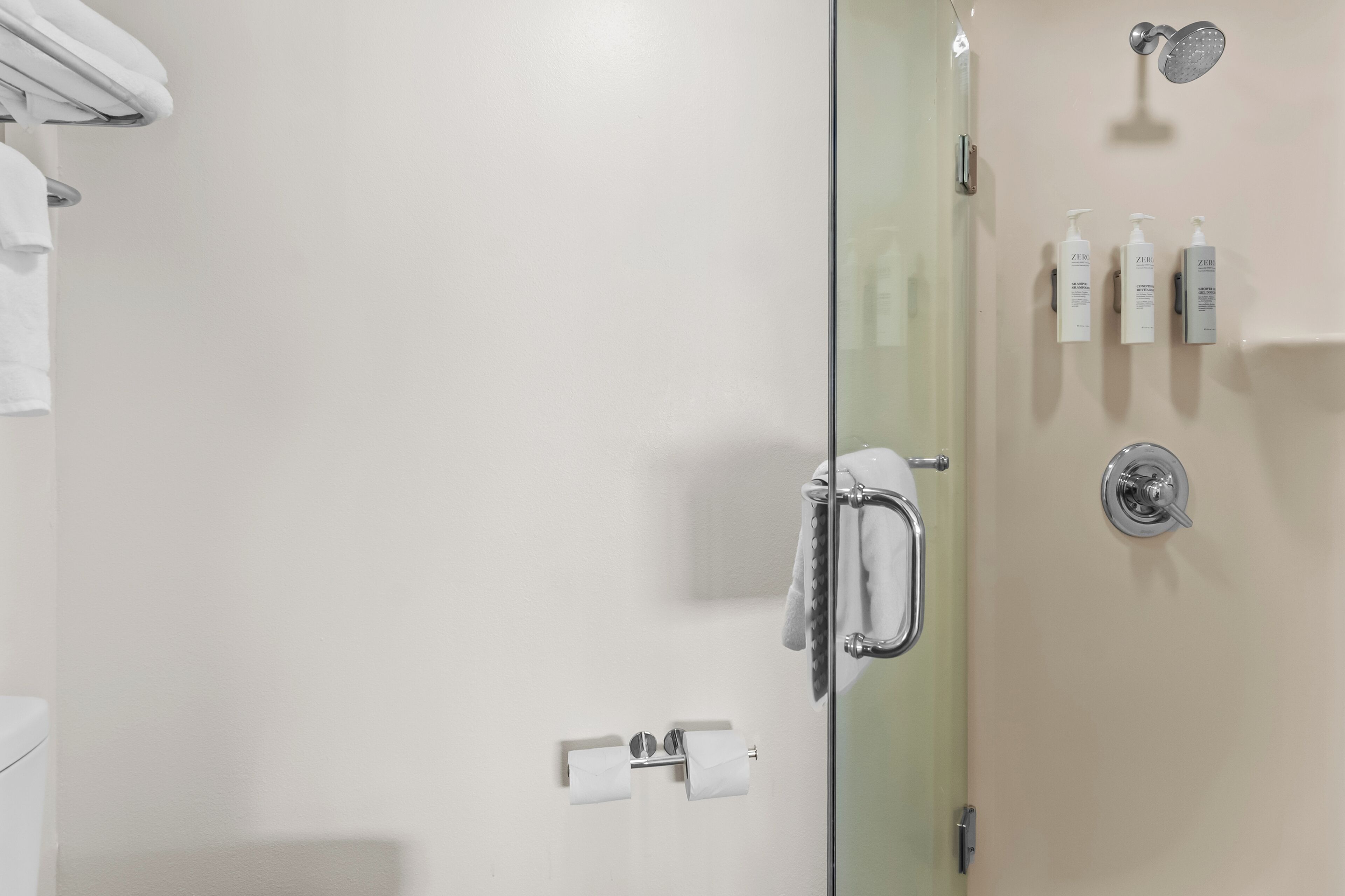 Un baño moderno con mampara de vidrio, toallero y artículos de aseo en la pared.