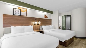 Une chambre d’hôtel avec deux lits, une tête de lit en bois, des lampes fixées au mur et des œuvres d’art encadrées.