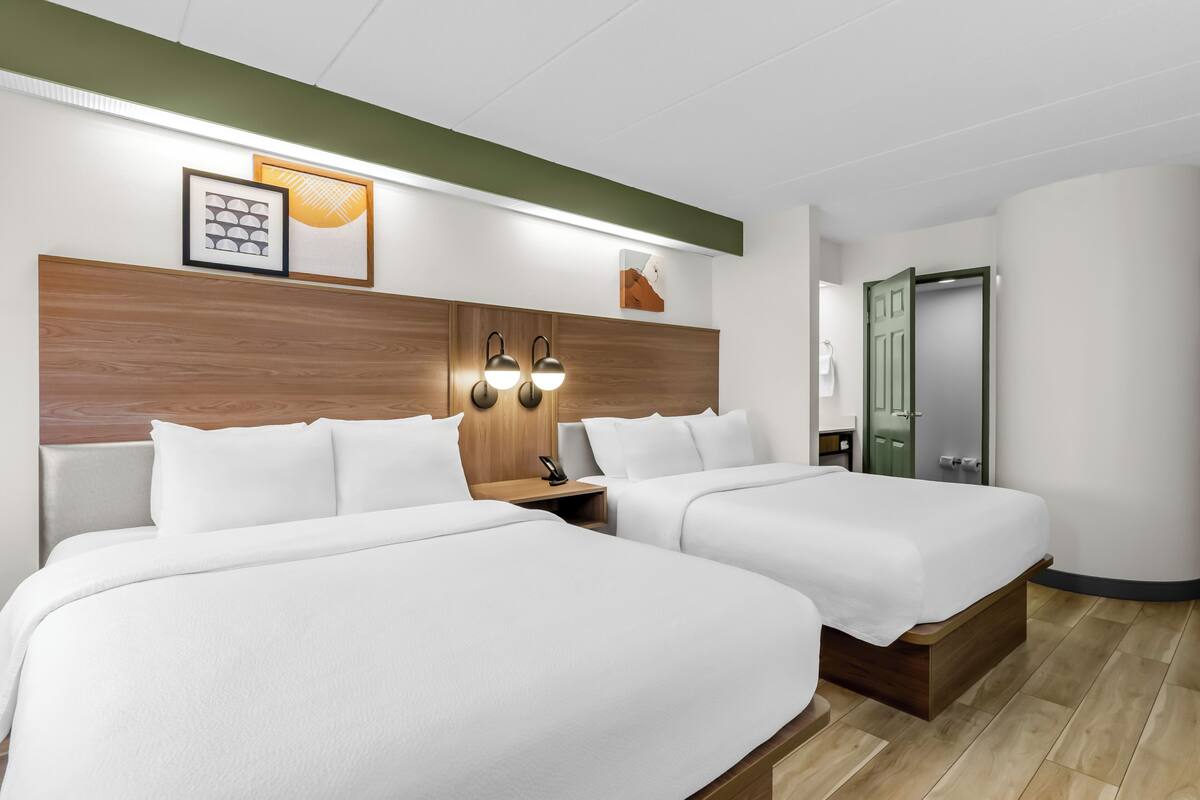 Une chambre d’hôtel avec deux lits, une tête de lit en bois, des lampes fixées au mur et des œuvres d’art encadrées.