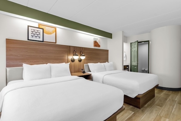 Habitación de hotel con dos camas, cabecero de madera, luces fijadas a la pared y cuadros enmarcados.