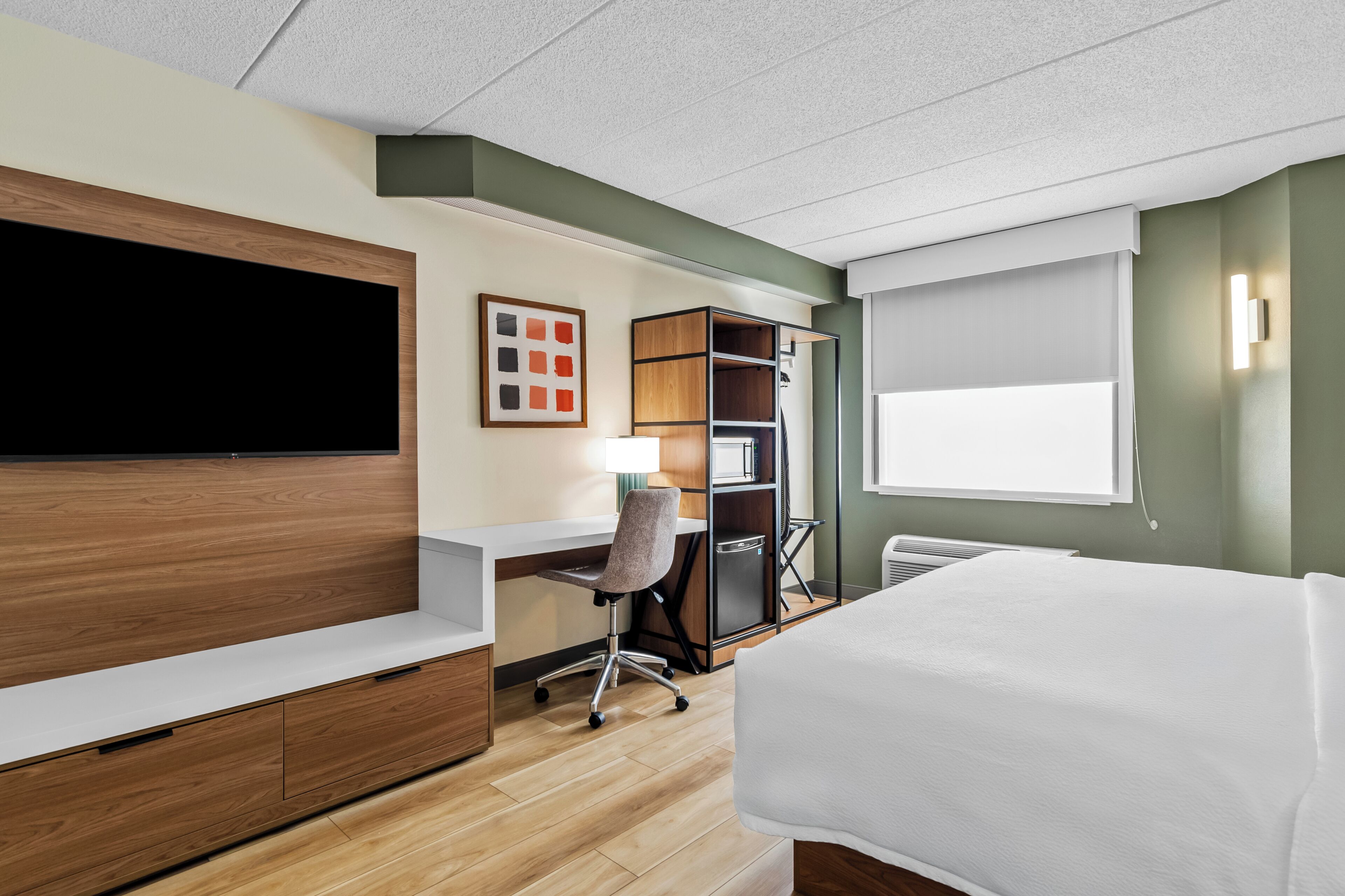 A hotel room with a bed, desk, chair, TV, wardrobe, and a window.