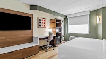 Habitación de hotel con cama, escritorio, silla, televisor, armario y ventana.