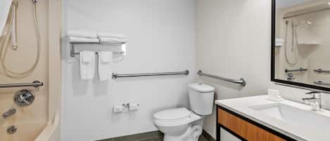 Un baño con bañera, inodoro y lavamanos, equipado con barras de apoyo y un secador de manos.