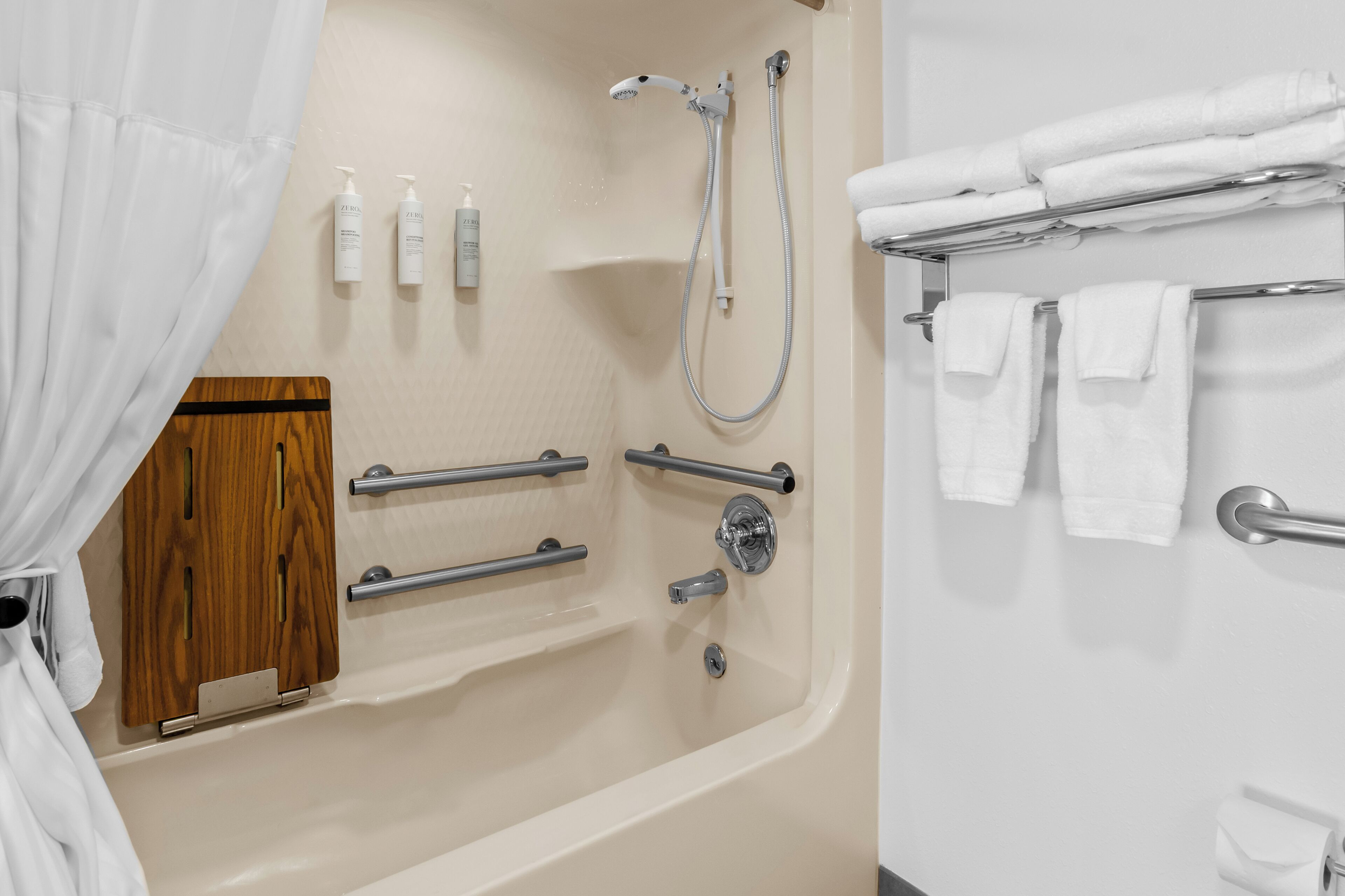 Un baño con bañera, ducha, barras de apoyo, un armario de madera y toallas ordenadas.