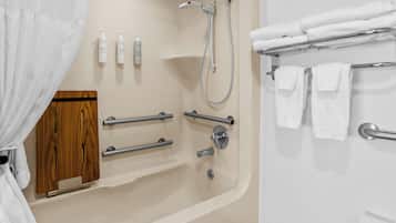 Un baño con bañera, ducha, barras de apoyo, un armario de madera y toallas ordenadas.