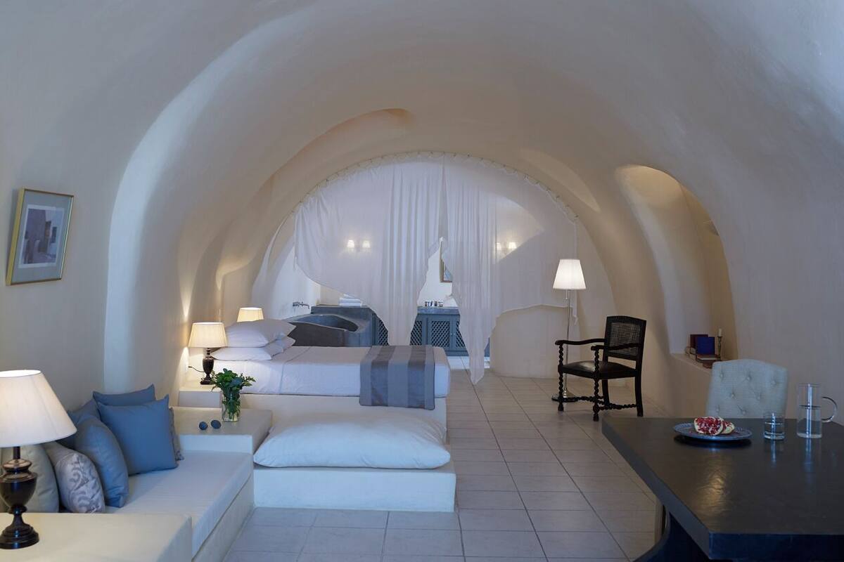 Une chambre d’hôtel moderne dotée d’un coin salon confortable, d’une table à manger et d’une grande porte en arc donnant sur une chambre à coucher.