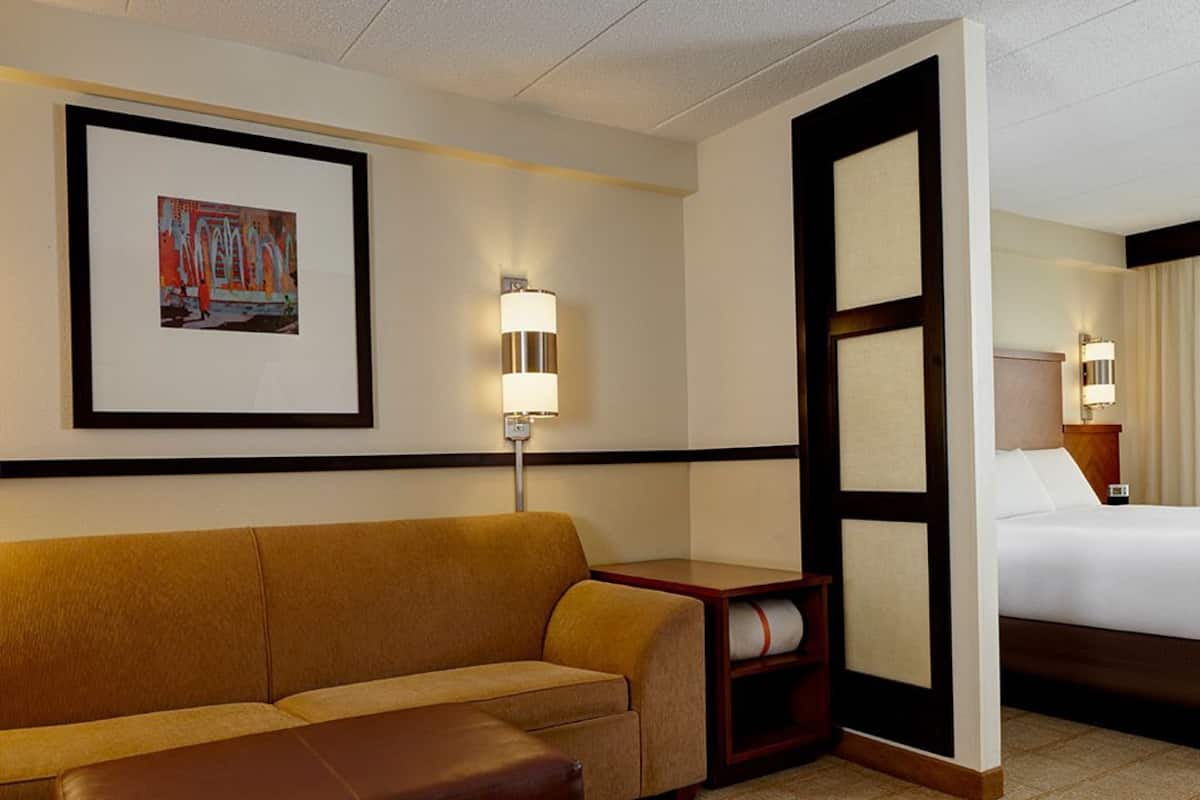 A hotel room with a sofa, a bed, a nightstand, and a framed picture on the wall.