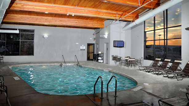 Una piscina interior con vigas de madera en el techo, un área de descanso junto a la piscina y grandes ventanales que ofrecen vistas a la puesta de sol.
