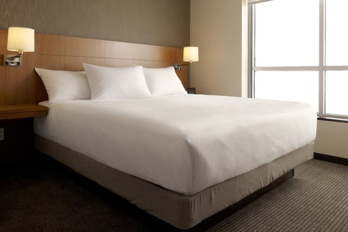 A neatly made bed with white linens, two bedside lamps, and a wooden headboard.