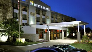 Un hotel de varios pisos con fachada moderna, un acceso cubierto y un asta de bandera.