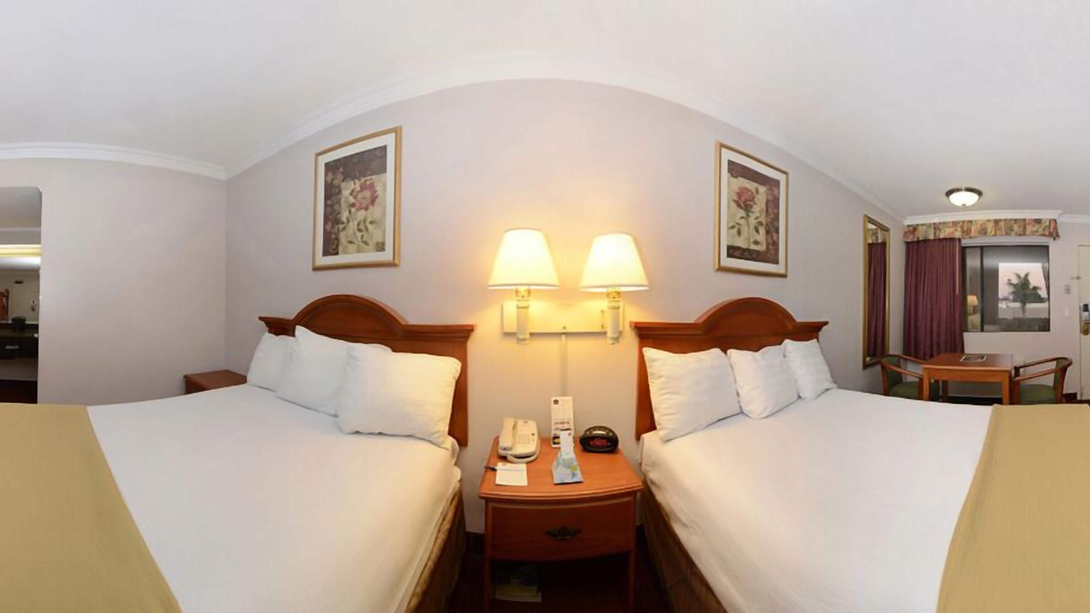 A hotel room with two single beds, a bedside table with a lamp, a telephone, and a small table with a chair.