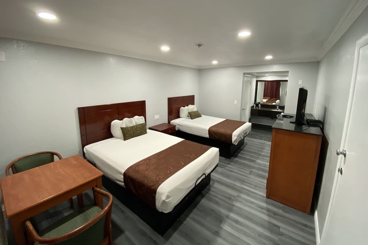 A hotel room with two beds, a desk, a chair, and a TV.