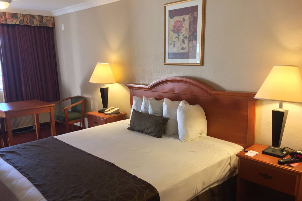 A hotel room with a large bed, two bedside tables, a desk, a chair, and two lamps.