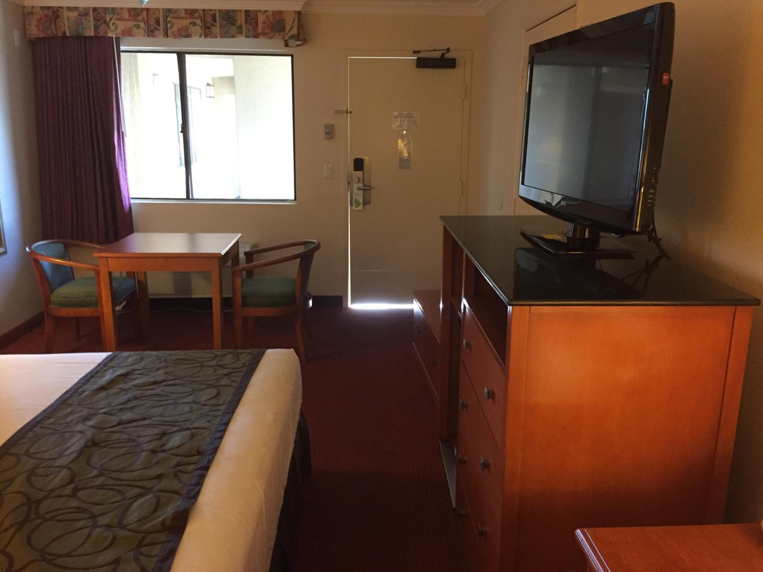 A hotel room with a bed, a desk, a television, and a door leading to a bathroom.