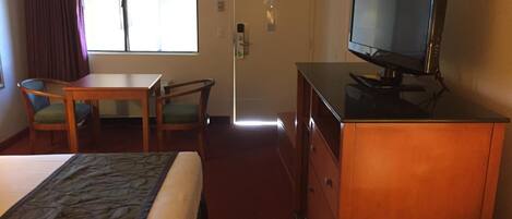 A hotel room with a bed, a desk, a television, and a door leading to a bathroom.
