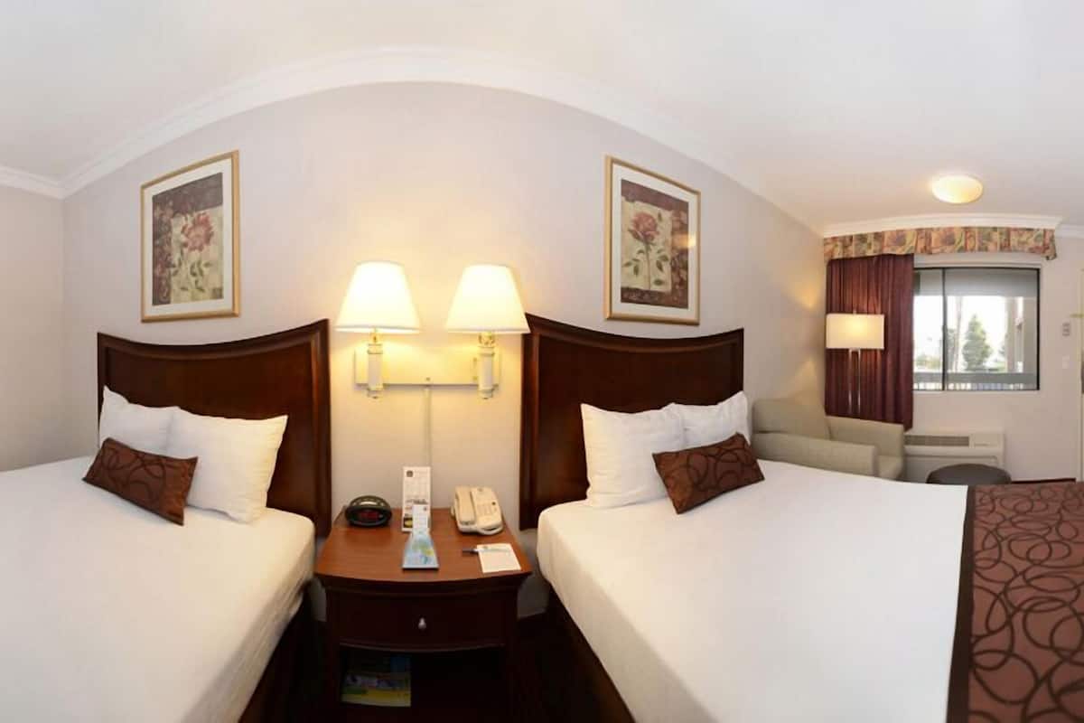 A hotel room with two beds, a nightstand, a lamp, and a window with curtains.