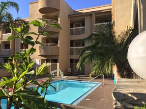 Un hotel a più piani con piscina, balconi e palme.
