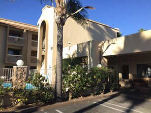 A building with a stone base, a palm tree, and a flower garden. - Chula Vista Inn (Chula Vista)