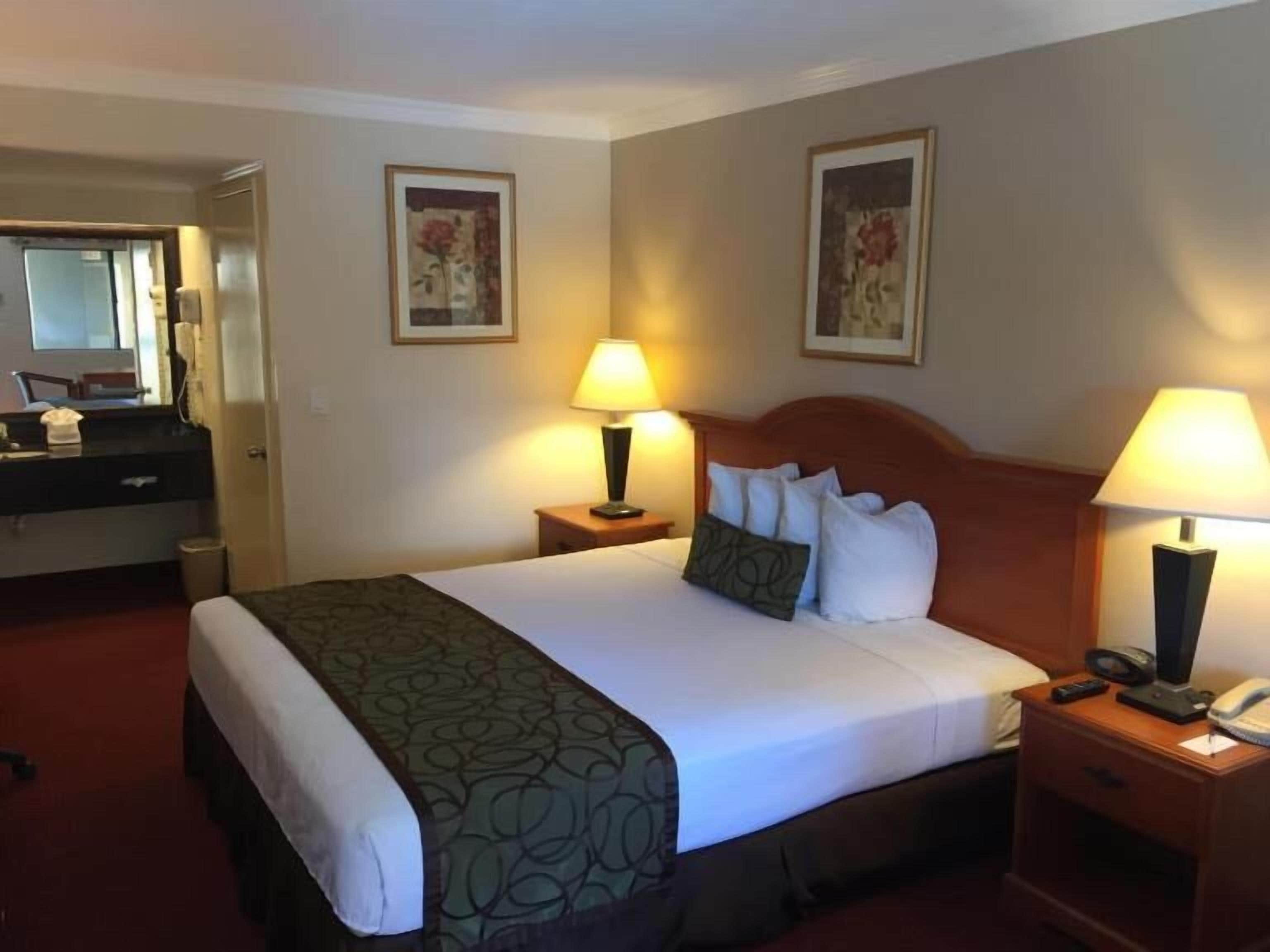 A hotel room with a bed, two bedside tables with lamps, a dresser, a mirror, and two framed pictures on the wall.