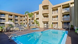 Ein Hotel mit Swimmingpool, Liegestühlen und einer Palme.