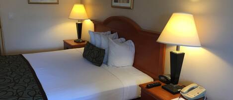 A neatly made bed with white linens and a green patterned throw, flanked by two bedside tables with lamps and a telephone.