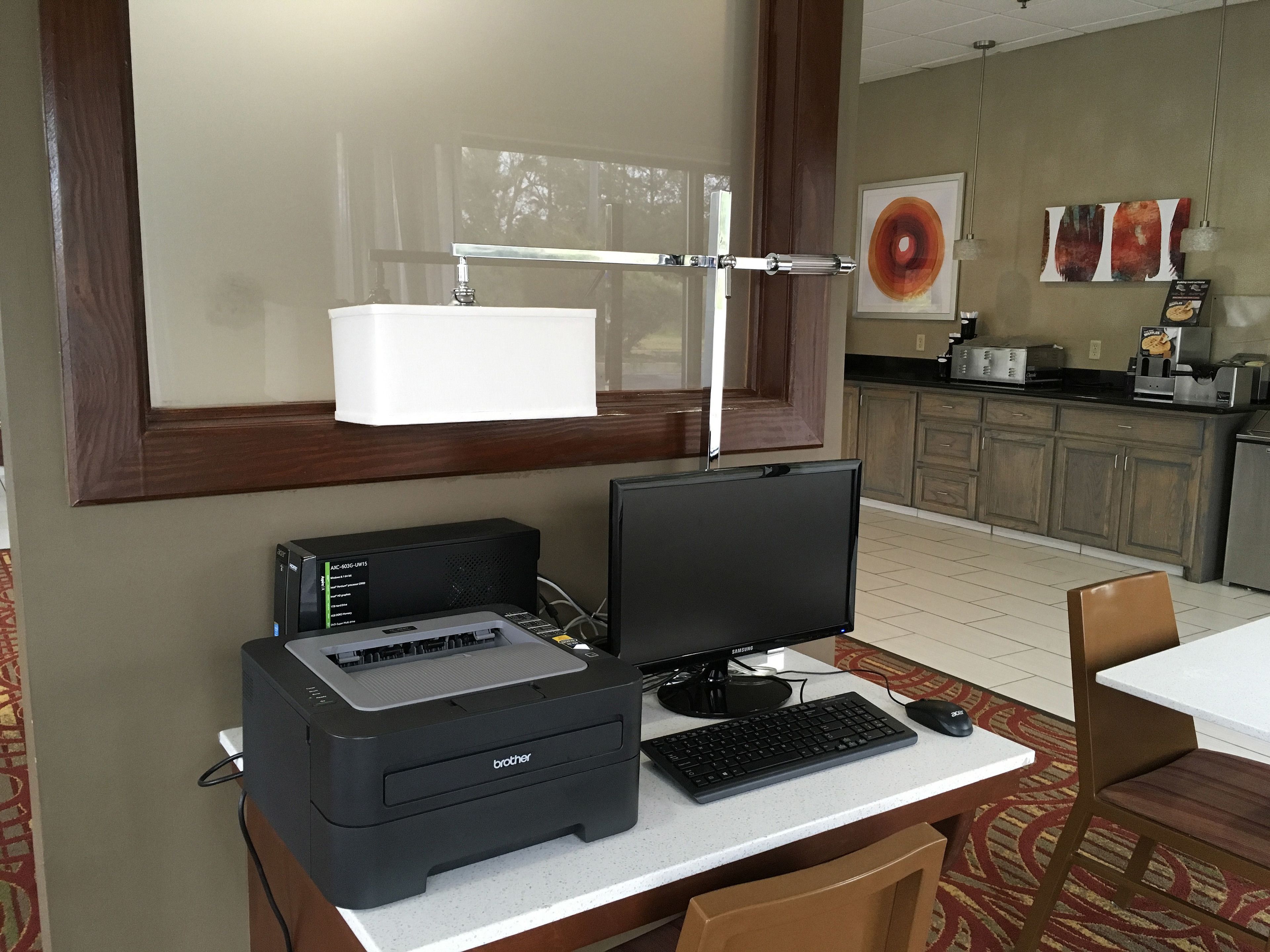 Habitación de hotel con escritorio, computadora de escritorio, impresora y una silla.