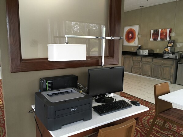 A hotel room with a desk, a desktop computer, a printer, and a chair.