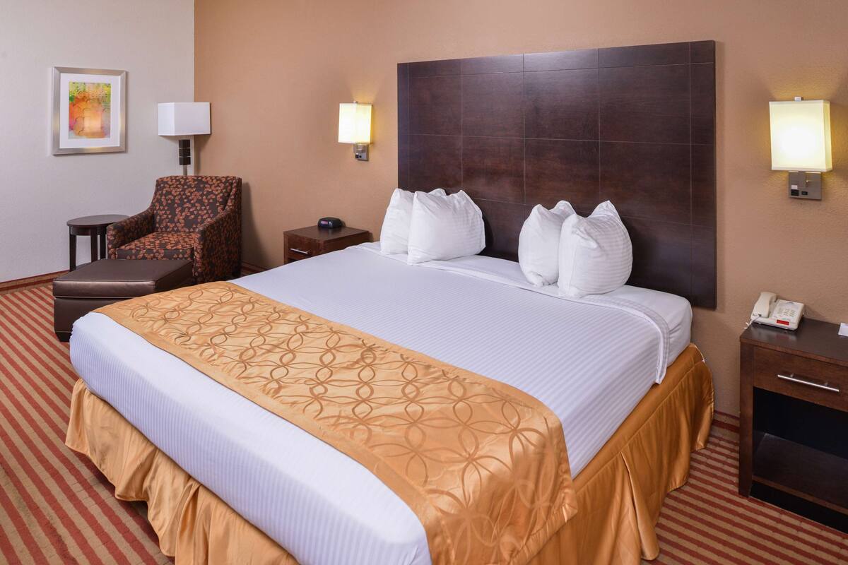 Une chambre d’hôtel avec un grand lit, une chaise, une table de chevet et une lampe.