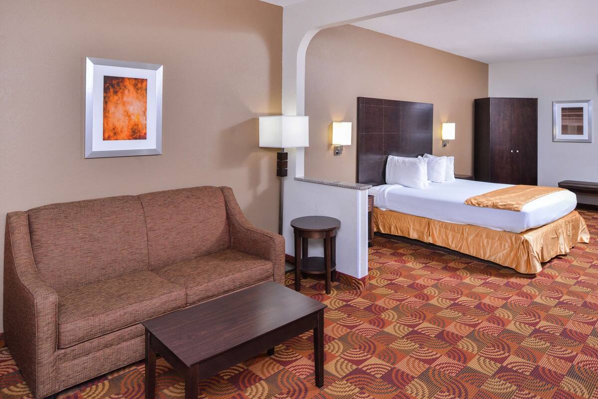 Une chambre d’hôtel avec un canapé, une petite table, un lit avec une tête de lit, un bureau et une lampe.