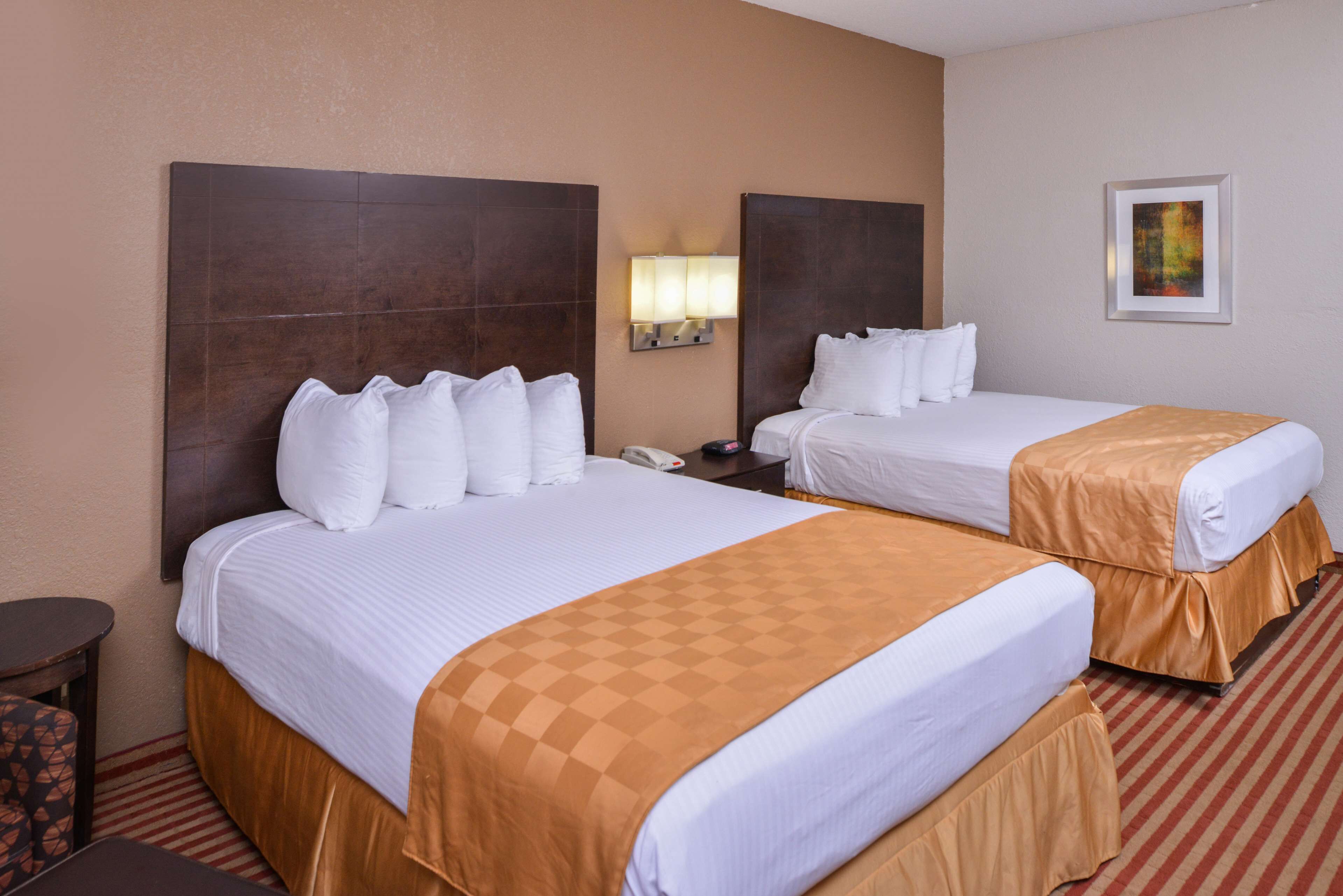 A hotel room with two beds, a nightstand, a lamp, and a framed picture on the wall.
