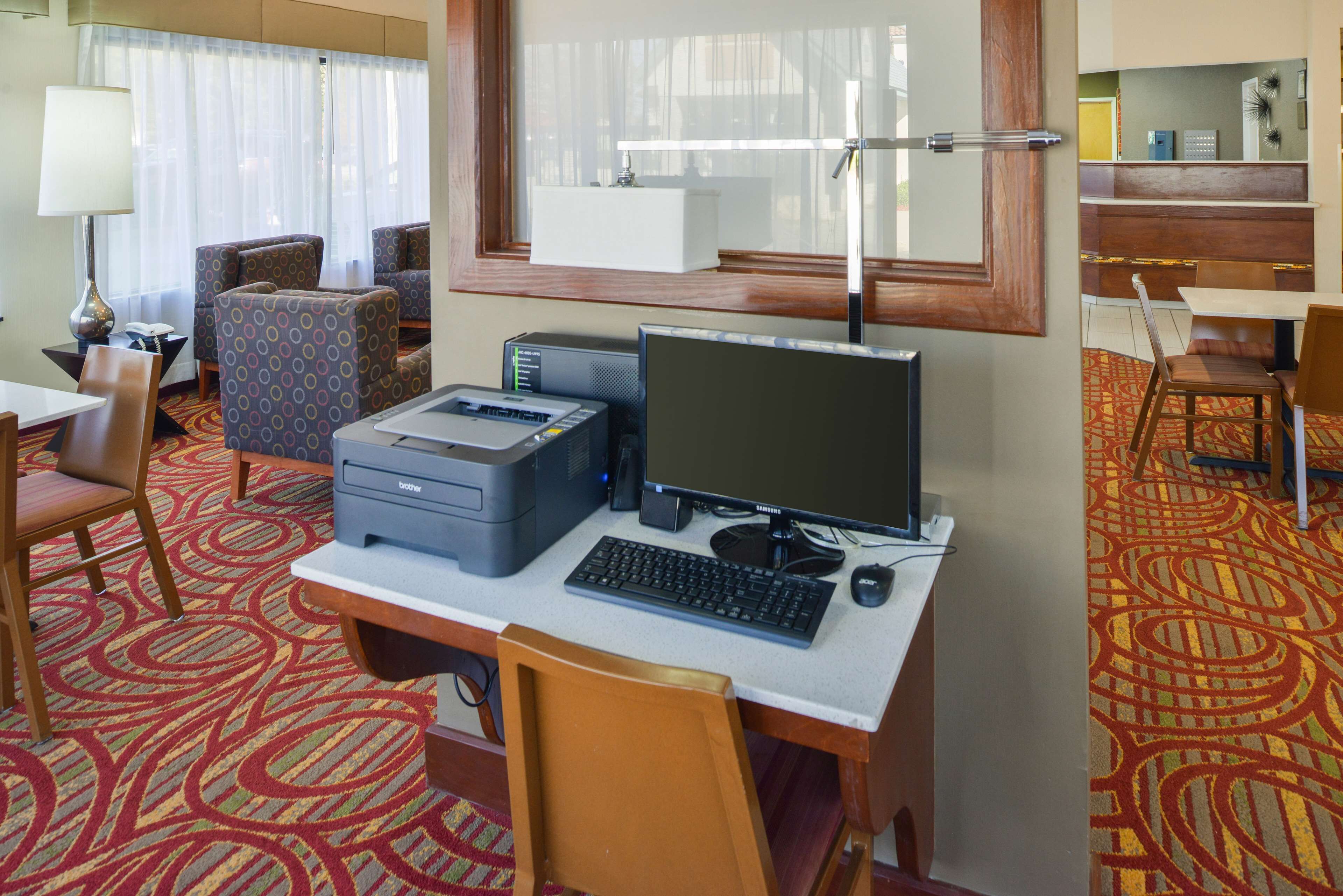 A hotel room with a desk, computer, printer, and seating area.