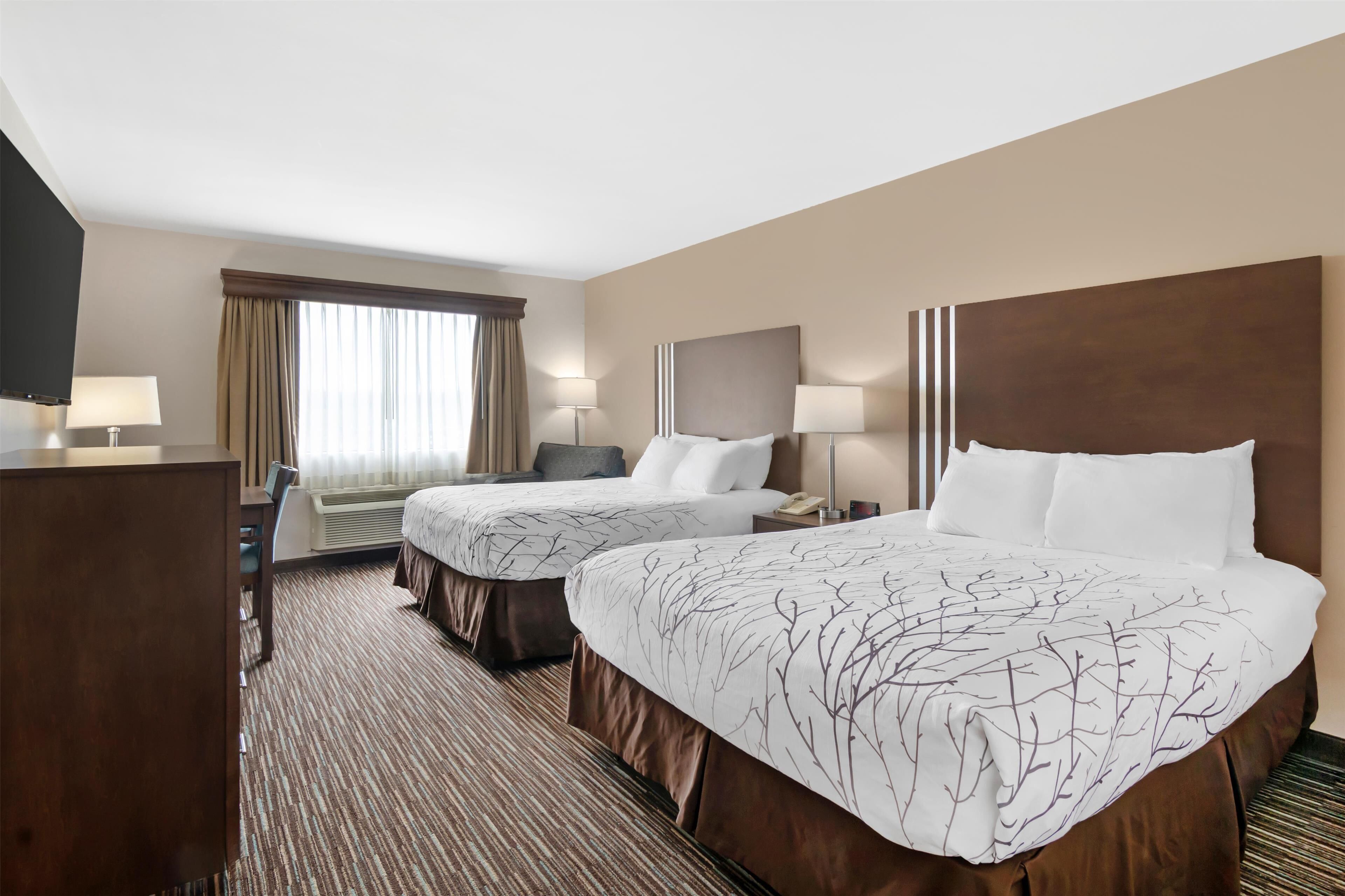 A hotel room with two beds, a desk, a chair, a TV, and a window with curtains.